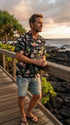 Pink Flamingo Hibiscus men's Hawaiian shirt in black, worn on a boardwalk at sunset